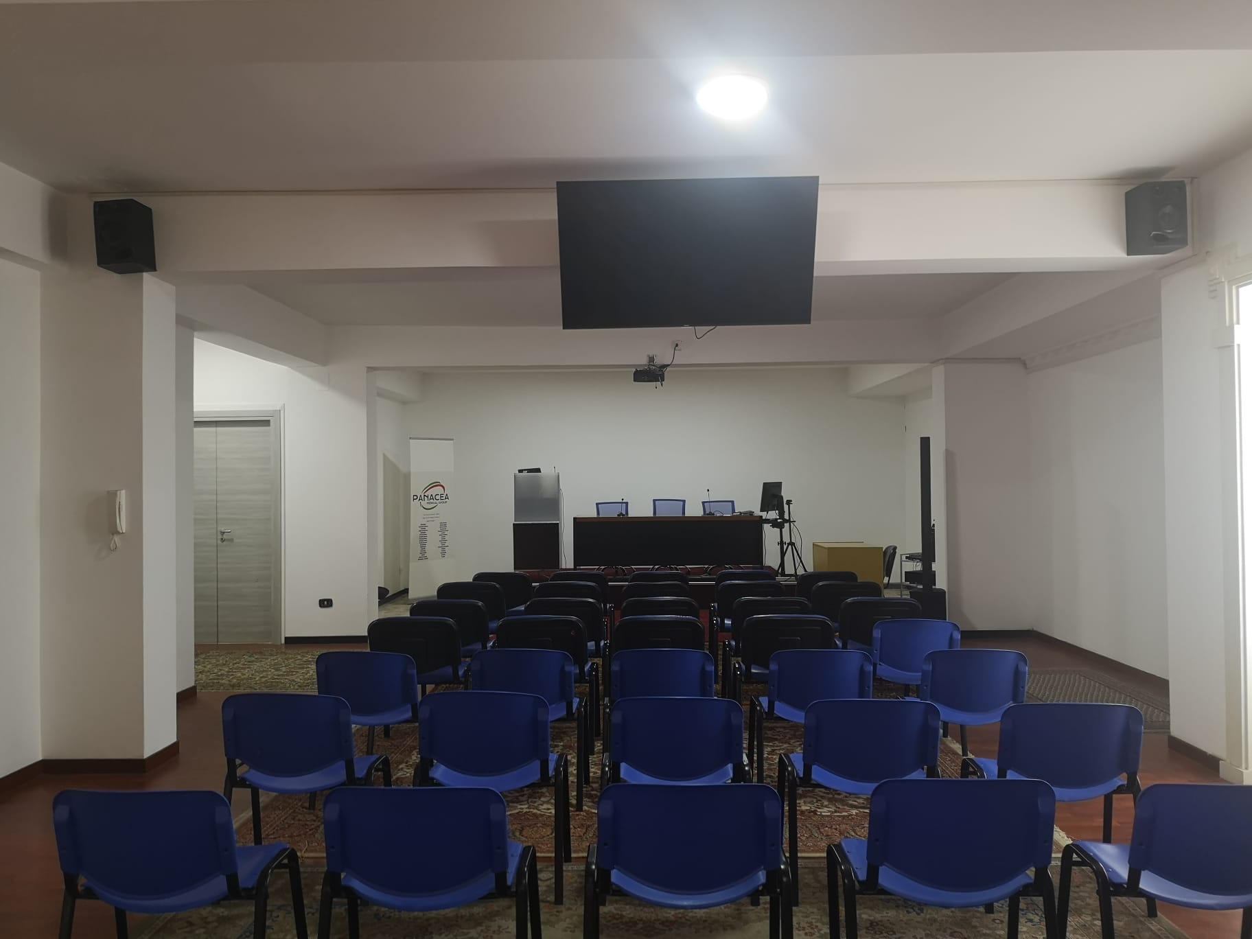 Sala convegni Panacea con maxi-schermo e tavolo relatori